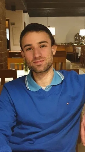 Man in blue sweater with light blue collar, sitting indoors in a restaurant.