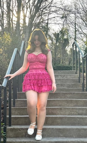 Curvy woman in pink dress on outdoor stairs.