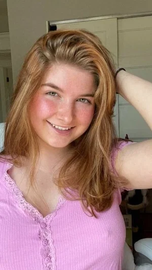 Woman with light brown hair in pink top, smiling indoors.