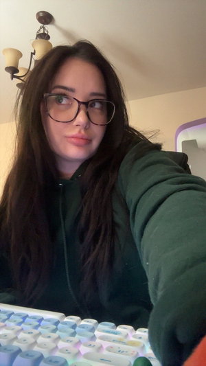 Woman with glasses and long dark hair in green hoodie indoors.