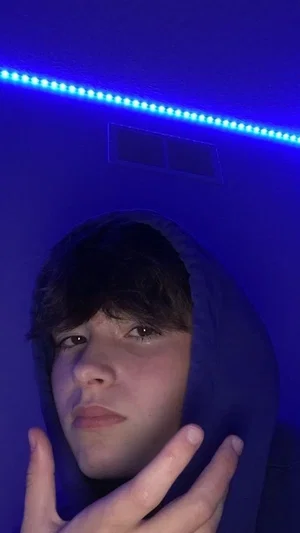 Person in dark hoodie under blue LED lights, hand near face, indoor setting.