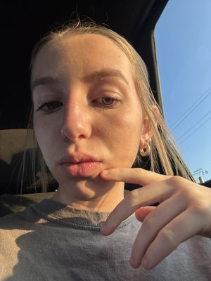 Woman with light hair in grey shirt taking selfie in car.