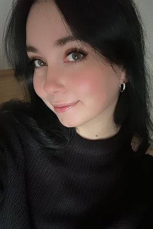 Woman with dark hair and makeup wearing a black top, smiling in a close-up selfie.