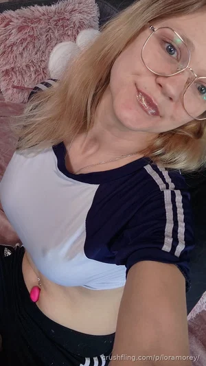 Woman with blonde hair and glasses in a crop top and black pants, taking a selfie indoors.