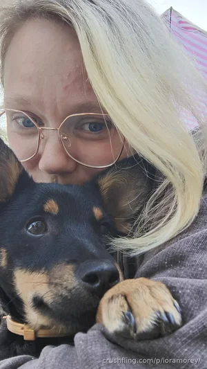 Blonde woman with glasses hugging a black and tan dog, wearing a gray sweater.