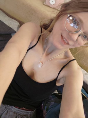 Woman with glasses in black tank top taking indoor selfie.