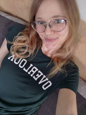 Woman with glasses and wavy hair wearing a black t-shirt, lying on a couch indoors.