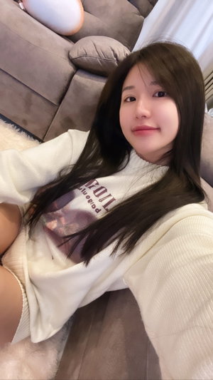 Woman with long dark hair in white sweater lying on couch indoors.