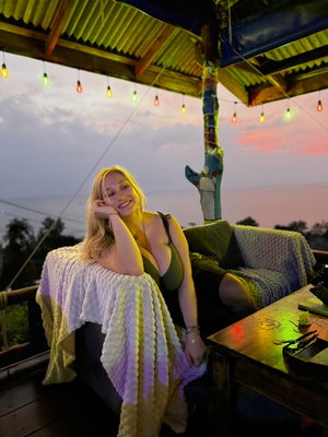 Blonde woman in green dress on outdoor couch at sunset.