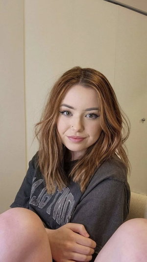 Woman with wavy brown hair wearing a dark t-shirt indoors.