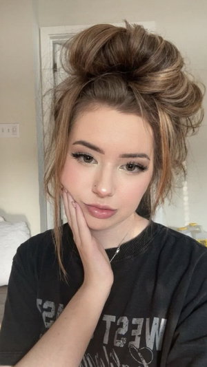 Brunette woman with hair in a bun wearing black t-shirt indoors.