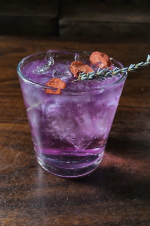 Purple cocktail with ice, dried fruit and lavender on wooden table.
