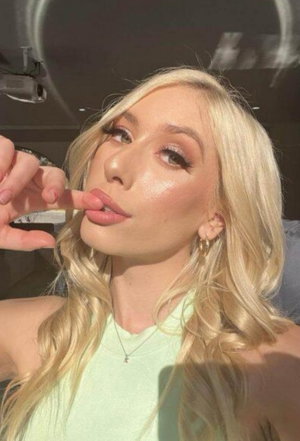 Blonde woman in light green top posing indoors, touching lips with finger.