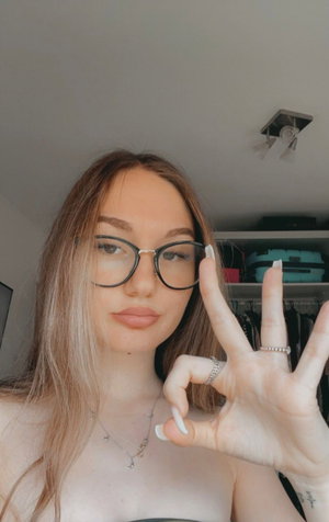 Woman with glasses, necklace making OK sign by closet.