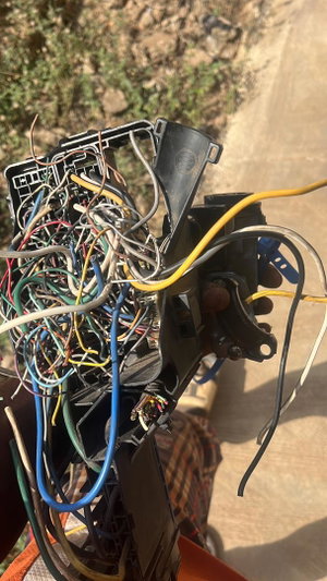 Hand holding tangled wires outdoors on dirt.