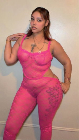 Curvy woman in pink sheer lingerie posing indoors.