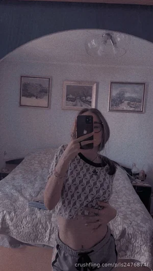 Woman in patterned crop top and shorts taking mirror selfie in bedroom.