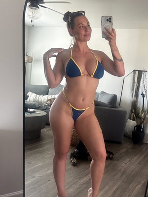 Woman in blue bikini taking mirror selfie in living room.