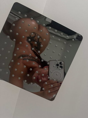 Woman with tattoos taking mirror selfie in bathroom.