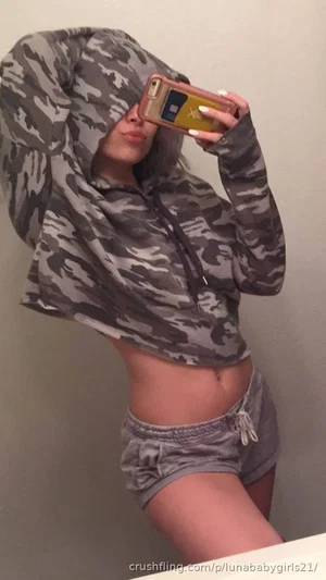 Woman in camo hoodie and shorts takes mirror selfie, showing midriff.