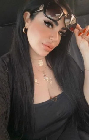 Woman with long black hair wearing black top and sunglasses in car.