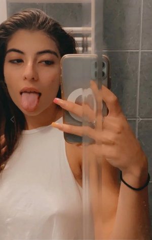 Dark-haired woman in wet white tank top bathroom selfie.