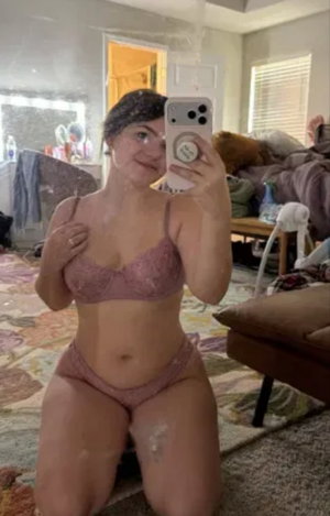 Woman in pink lingerie taking a selfie indoors.