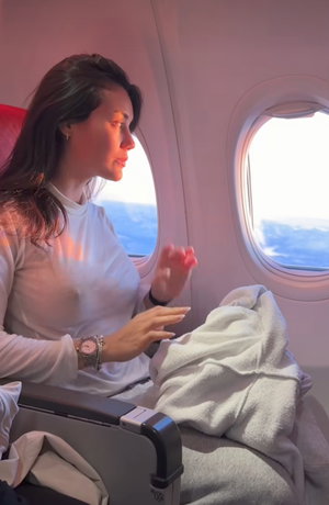 Woman in sheer white top seated by airplane window.