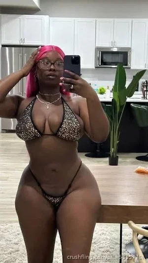 Woman with pink hair in leopard print lingerie taking mirror selfie in kitchen.
