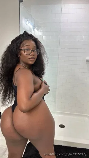 Woman with curly hair in black lingerie posing in bathroom, hand on chest.