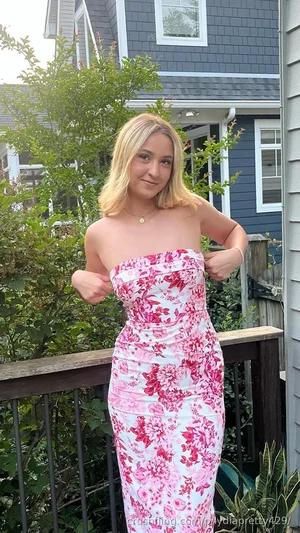 Woman in floral strapless dress standing on outdoor deck, blonde hair, smiling.