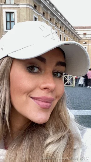 Woman with blonde hair and white cap smiling in outdoor urban setting.