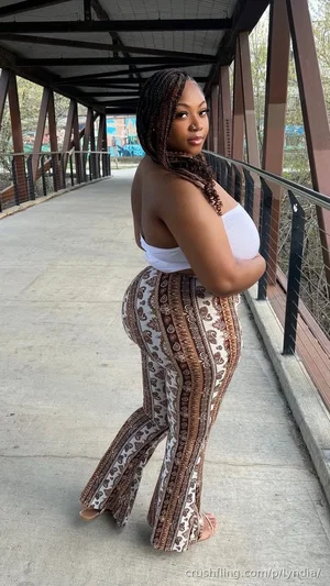 Woman with braided hair in white top and patterned pants on a covered bridge.