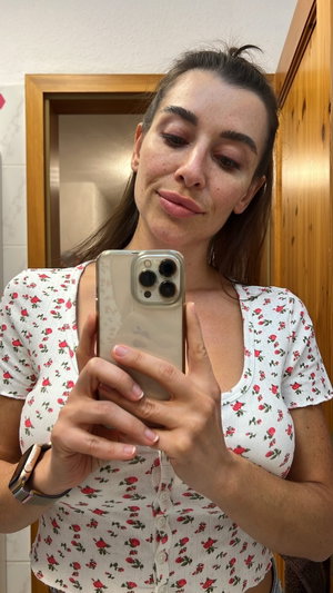 Woman in floral top taking bathroom mirror selfie.