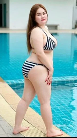 Woman in striped bikini posing by poolside, curvy figure, outdoor setting.