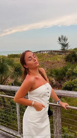 Woman in white strapless dress leaning on railing outdoors near ocean.