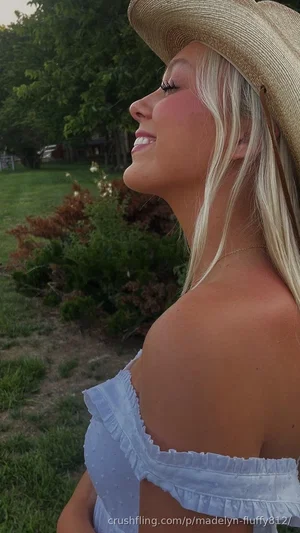 Blonde woman in straw hat and light blue off-shoulder top, outdoors in garden.