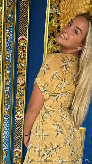 Blonde woman in yellow floral dress posing near ornate blue and gold door.