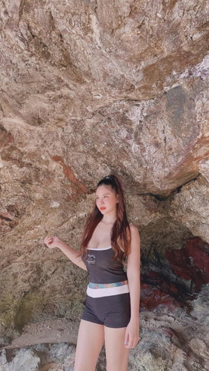 Woman with long hair in gray top and shorts near rocks.