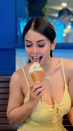 Woman in yellow top eating ice cream indoors.