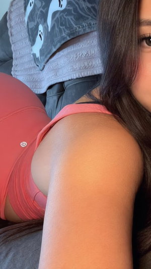 Woman with long dark hair in pink sports bra, sitting indoors near gray blanket.