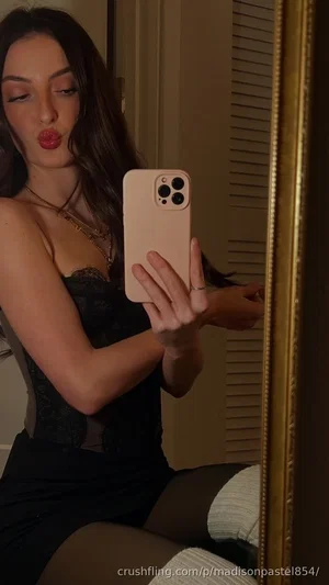 Woman in black lace top and white thigh-highs takes mirror selfie in bedroom.