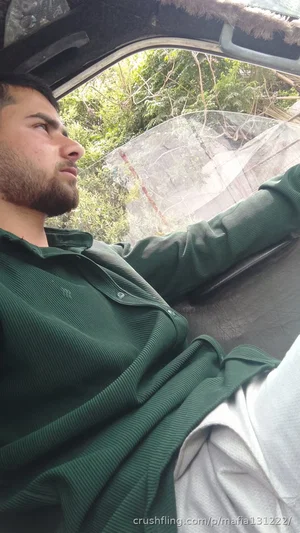 Man in green shirt sitting in vehicle, looking out window, outdoor background.