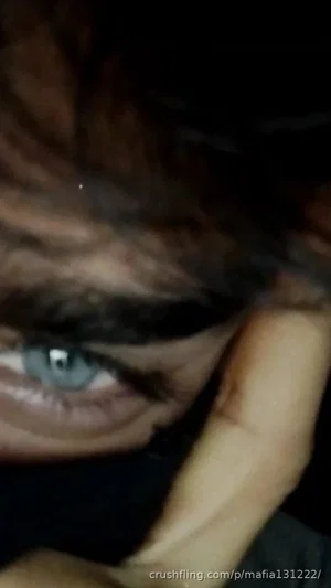 Close-up of a person's eye with dark hair, hand near face, dim lighting.