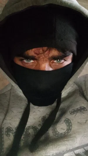 Person in gray hoodie and black face covering, eyes visible, indoor setting.
