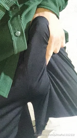 Person in green ribbed shirt and black pants, hand on hip, indoor setting.