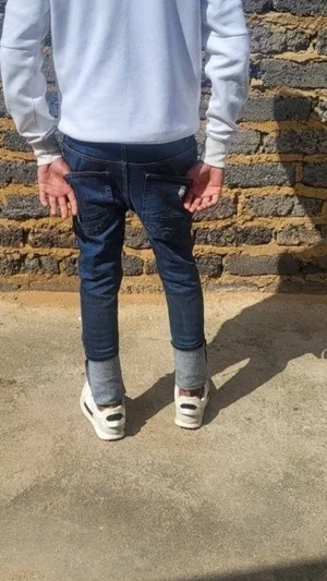 Person in white sweatshirt and jeans standing outdoors near stone wall.