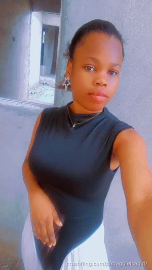 Woman in black sleeveless top and white skirt, standing indoors near a concrete wall.