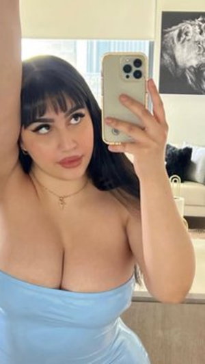 Woman in light blue strapless dress taking mirror selfie indoors.