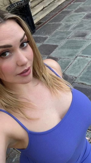 Woman with blonde hair in blue tank top, outdoors on stone pavement.